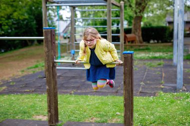 Küçük kız tırmanma iskeletinde jimnastik yapıyor, okul bahçesinde yatay bar. Çocuk okul tatilinde eğleniyor