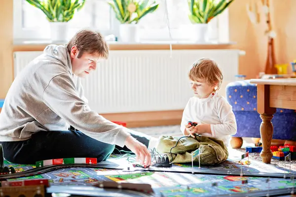 Baba ve oğul yarış arabalarıyla yarış pistinde, kapalı alanda, arabalarla oynuyorlar. Küçük mutlu anaokulu çocuğu ve genç adam kapalı alandaki yarış oyunlarıyla eğleniyor.