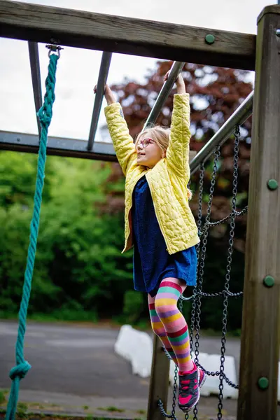 Küçük kız tırmanma iskeletinde jimnastik yapıyor, okul bahçesinde yatay bar. Çocuk okul tatilinde eğleniyor