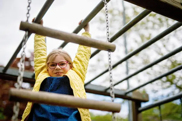 Küçük kız tırmanma iskeletinde jimnastik yapıyor, okul bahçesinde yatay bar. Çocuk okul tatilinde eğleniyor