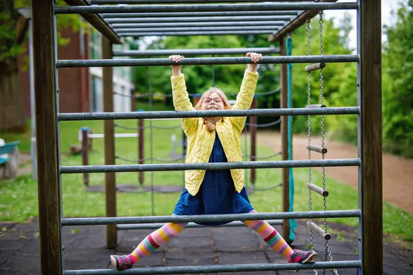 Küçük kız tırmanma iskeletinde jimnastik yapıyor, okul bahçesinde yatay bar. Çocuk okul tatilinde eğleniyor