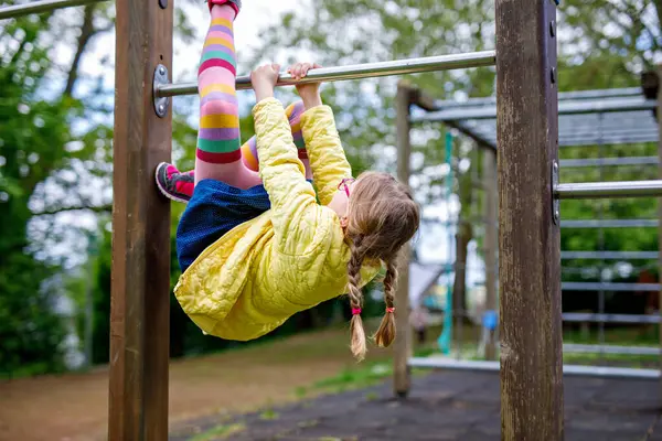 Küçük kız tırmanma iskeletinde jimnastik yapıyor, okul bahçesinde yatay bar. Çocuk okul tatilinde eğleniyor