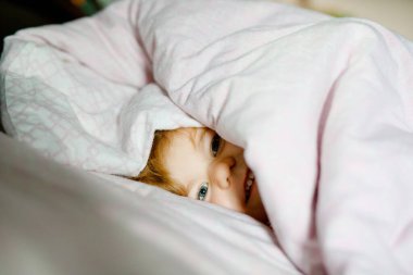 Küçük kız uyandıktan sonra yatakta eğleniyor. Sağlıklı çocuklar atlayıp aileleriyle saklambaç oynarlar. Evdeki sevimli çocuk, aile hayatı.