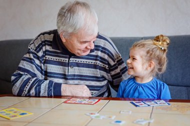 Güzel küçük kız ve büyükbaba evde resim masası kart oyunu oynuyorlar. Tatlı çocuk ve son sınıf öğrencisi birlikte eğleniyor. Mutlu aile içeride..