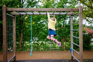 Küçük kız tırmanma iskeletinde jimnastik yapıyor, okul bahçesinde yatay bar. Çocuk okul tatilinde eğleniyor