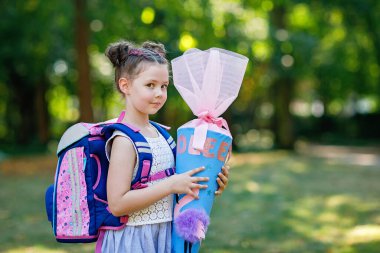 Sırt çantası, çantası ve büyük okul çantası olan mutlu küçük bir kız çocuğu ya da okulun ilk günü için Almanya 'da geleneksel Schultuete adı verilen bir koni. Yeni öğrenci, okula geri dön.