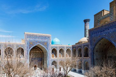 Semerkand, Özbekistan 'daki Registan Meydanı' nın bir parçası, parlak mavi gökyüzü altında karmaşık mozaik tasarımlar, kubbeler ve minareler içeren üç çarpıcı medresenin yer aldığı tarihi bir mimari grup..