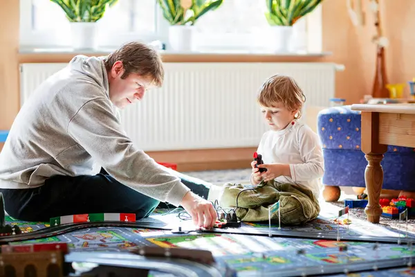 Baba ve oğul yarış arabalarıyla yarış pistinde, kapalı alanda, arabalarla oynuyorlar. Küçük mutlu anaokulu çocuğu ve genç adam kapalı alandaki yarış oyunlarıyla eğleniyor.