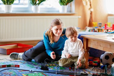 Anne ve oğlu yarış arabalarıyla yarış pistinde, kapalı alanda, arabalarla oynuyorlar. Küçük mutlu anaokulu çocuğu ve genç kadın kapalı alandaki yarış oyunlarıyla eğleniyorlar.