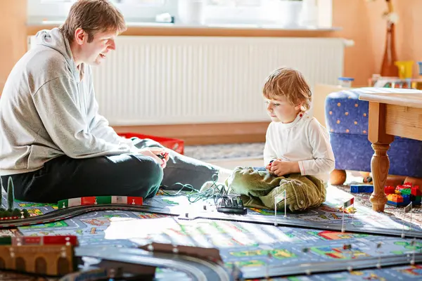 Baba ve oğul yarış arabalarıyla yarış pistinde, kapalı alanda, arabalarla oynuyorlar. Küçük mutlu anaokulu çocuğu ve genç adam kapalı alandaki yarış oyunlarıyla eğleniyor.