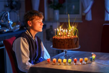 Sevimli mutlu ergen çocuk doğum gününü kutluyor. Genç bir çocuk ev yapımı pastaya 14 mum üflüyor. Okul çocukları için doğum günü partisi, aile kutlaması, ergen doğum günü..