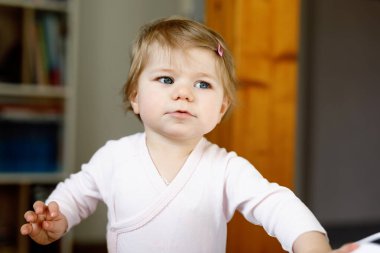 Küçük kız yürümeyi öğreniyor, ayakta duruyor ve evde ilk adımlarını atıyor. Yürümeye başlayan çocuk dengede duruyor. Mutlu çocuk, denge ve gelişme.