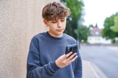 Elinde akıllı telefon tutan gülümseyen ergen okul çocuğunun portresi. Mutlu ergen çocuk video görüşmesinde arkadaşlarıyla konuşuyor, kameraya güvenle bakıyor. Gerçek hayat, gerçek insanlar, gençlik yaşam tarzı konsepti