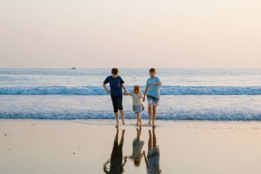Üç çocuk, gün batımında okyanus sahilinde mutlu kardeşler. Mutlu bir aile, iki okul çocuğu ve küçük bir anaokulu kızı. Kardeşler eğleniyor, İspanya, Costa del Sol