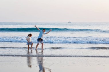 Okyanus sahilinde iki çocuk. Ergen çocuk ve anaokulu kız kardeşi gün batımında eğleniyorlar. Aile için deniz tatili. Kardeşler gülüyor ve gülüyor. Mutluluk ve aşk