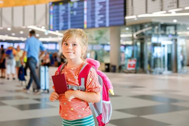 Havaalanı terminalindeki küçük anaokulu kızı. Mutlu çocuk uçakla tatile çıkıyor. Pasaportu ve çantası olan gülümseyen çocuk.