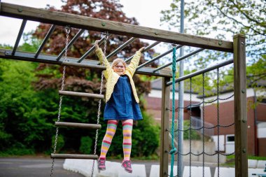 Küçük kız tırmanma iskeletinde jimnastik yapıyor, okul bahçesinde yatay bar. Çocuk okul tatilinde eğleniyor