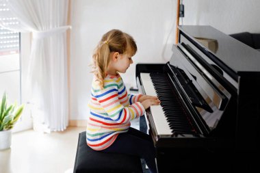Oturma odasında piyano çalan güzel küçük kız. Evde Corona virüsü kilitleme sırasında öğrenme konseptiyle müzik aleti çalmayı öğrenmekle eğlenen sevimli anaokulu çocuğu.