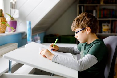 Gözlüklü çocuk okul için evde öğreniyor. Çocuk ev ödevi yapıyor. Evde eğitim ve uzaklık öğrenme kavramı