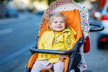 Bebek arabasında ya da bebek arabasında oturan ve yürüyüşe çıkan küçük tatlı bir kızın portresi. Mutlu şirin bebek dışarıda eğleniyor. Sağlıklı bir kız. Şehirde sokak trafiği