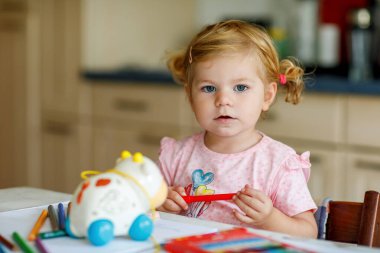 Kalemle resim yapmayı öğrenen sevimli bir bebek. Küçük çocuk renkli keçeli kalemlerle evde resim çiziyor. Evde ya da çocuk odasında renkler deneyen sağlıklı, mutlu bir kız.