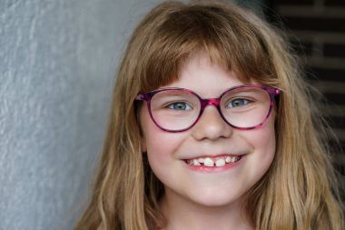 Sevimli, mutlu, gülümseyen, gözlüklü ve uzun sarı saçlı ilkokul kızının portresi. Gerçek hayat, gerçek insanlar, doğal çocukluk sevinci ve kendine güveni..