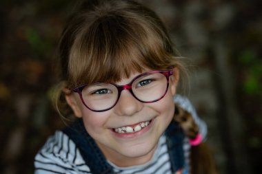Sevimli, mutlu, gülümseyen, gözlüklü ve uzun sarı saçlı ilkokul kızının portresi. Gerçek hayat, gerçek insanlar, doğal çocukluk sevinci ve kendine güveni..