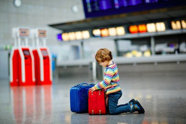 Uluslararası havaalanındaki terminalde büyük bavulları olan küçük mutlu çocuk. Okul öncesi heyecanlı çocuk uçuşu ve tatile çıkmayı bekliyor. Seyahat aile hayatı.