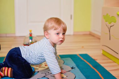 Küçük çocuk oyun odasında emekliyor, oyuncaklarla oynuyor. Mutlu bebek içeride eğleniyor. Gerçek hayat, gerçek insanlar, çocukluk, gelişme, oyun zamanı, öğrenme, neşe