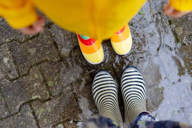 Anne ve çocuğun yağmurda yürürken çekilmiş lastik çizmeleri. Aile dışarıda yağmurlu havanın keyfini çıkarıyor. Gerçek hayat, gerçek insanlar.