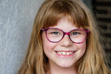 Sevimli, mutlu, gülümseyen, gözlüklü ve uzun sarı saçlı ilkokul kızının portresi. Gerçek hayat, gerçek insanlar, doğal çocukluk sevinci ve kendine güveni..