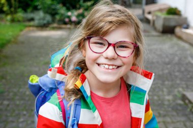 Gözlüklü ve sırt çantalı şirin bir ilkokul öğrencisi okula giderken yolda yürüyor. Gülümseyen öğrenci okula, eğitime ve çocukluk yaşam tarzı konseptine hazır..