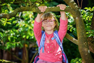 Gözlüklü ve sırt çantalı şirin bir ilkokul öğrencisi okula giderken yolda yürüyor. Gülümseyen öğrenci okula, eğitime ve çocukluk yaşam tarzı konseptine hazır..