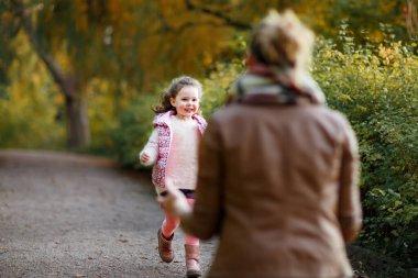 Anne ve kızı sonbahar parkında birlikte yürüyorlar. Mutlu aile, sonbahar sezonunu dışarıda geçiriyor. Gerçek hayat, gerçek insanlar..