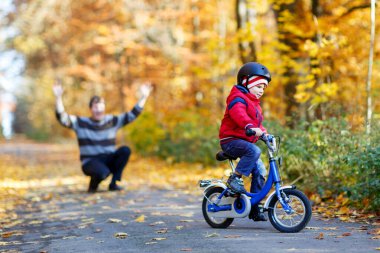Sonbahar parkında bisikletli bir çocuk ve babası. Baba oğluna bisiklete binmeyi öğretiyor. Aktif aile eğlencesi. Bisikletli kasklı çocuk. Güvenlik, spor, çocuk konseptiyle eğlence..
