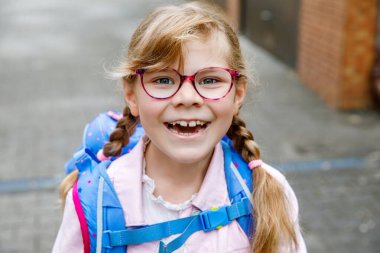 Gözlüklü ve sırt çantalı mutlu bir ilkokul öğrencisi okula giderken yolda yürüyor. Gülümseyen öğrenci okula, eğitime ve çocukluk yaşam tarzı konseptine hazır..