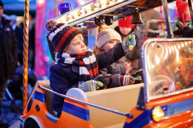Sevimli küçük erkek ve kız, Noel funfair veya pazar, açık havada bir atlıkarınca üzerinde kardeşler. Mutlu çocuklar, arkadaşlar eğleniyor. Bir çocuğa seçici bir odaklanma. Tatil, çocuklar, yaşam tarzı kavramı.