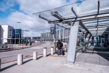 Stavanger, Norveç, 14 Mart 2023, Sola Havaalanı Stavanger 'ında güneşli bir kış gününde ana terminal binasının önünde otobüs bekleyen iki kişi.