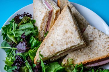 Londra İngiltere, 14 Temmuz 2025, Ev yapımı jambonlu ve peynirli sandviç dilimlenmiş kahverengi ekmek ve yeşil salata yaprakları