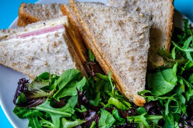 Londra İngiltere, 14 Temmuz 2025, Ev yapımı jambonlu ve peynirli sandviç dilimlenmiş kahverengi ekmek ve yeşil salata yaprakları