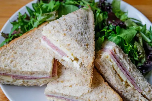Londra İngiltere, 14 Temmuz 2025, Ev yapımı jambonlu ve peynirli sandviç dilimlenmiş kahverengi ekmek ve yeşil salata yaprakları