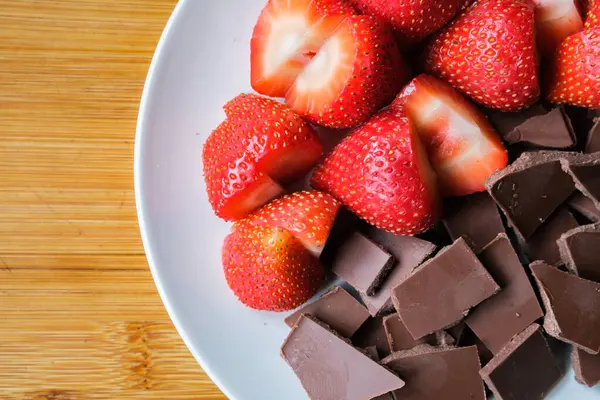 Londra İngiltere, 15 Temmuz 2025, Dilimlenmiş taze organik çilekler Kırık Süt Çikolatası ile