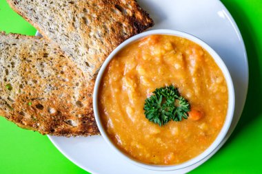 Londra İngiltere, 16 Temmuz 2025, Maydanozla süslenmiş bir kase sıcak vejetaryen mercimek çorbası