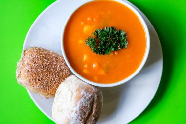 Londra İngiltere, 16 Temmuz 2025, maydanozla süslenmiş bir kase sağlıklı sebze çorbası ve yumuşak ekmek rulosu.