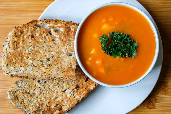 Londra İngiltere, 16 Temmuz 2025, maydanozla süslenmiş ve kızarmış ekmekle servis edilen bir kase sağlıklı sebze çorbası.