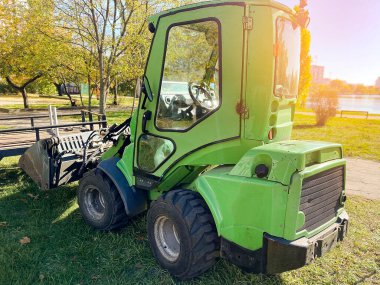 Modern tekerlek yükleme makinesi, parktaki çimlerin üzerinde traktör. Belediye rekonstrüksiyon, yenilenen şehir dinlenme alanı üzerinde çalışıyor. Ağır, hafif makine kiralama. İlkbaharda tarla sürme.