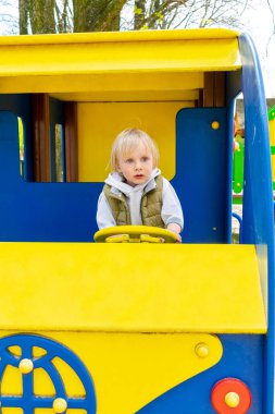 Tatlı, komik, sarışın, küçük çocuk. Oyuncak arabada, otobüste, çocuk parkında oturuyor. Çocuklar fiziksel, duygusal gelişim ve çocukluk bakımı, anaokulu kavramı..