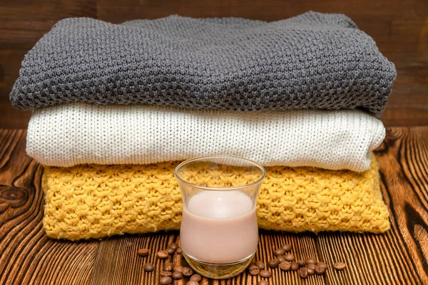 Home wardrobe with winter clothes. Stack of folded cashmere warm woolen knitted sweaters clothes. Autumn, winter cold season knitwear on wooden table with hot cacao latte beverage.