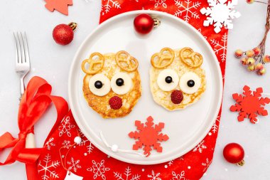 Christmas deers face shaped pancake with sweet fresh raspberry berry and cheese on plate for kids baby children breakfast dinner. xmas food with new year decorations on gray background close up.