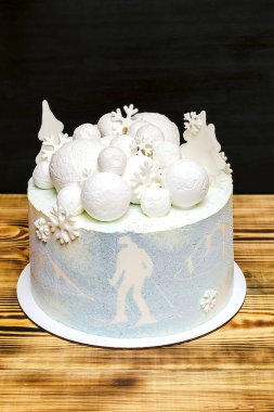 Beyaz mavi hindistan cevizi lezzetli vanilyalı kremalı pasta büyük yuvarlak marşmelov, çikolata kar taneleri, köknar ağaçları, dağ ve kayak resmi, ahşap masa üzerindeki tatlı tatlı tatlı tatlı.